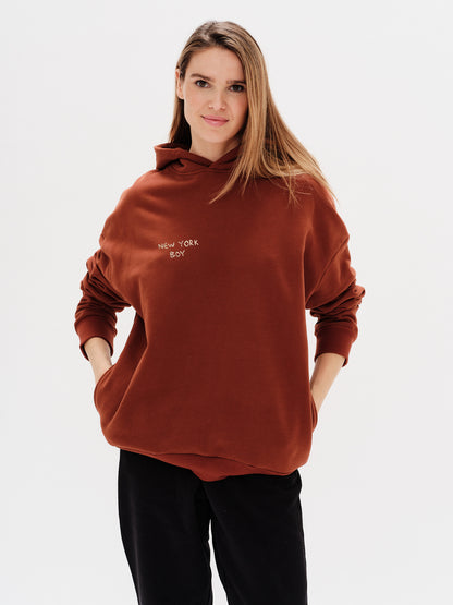 Woman wearing a brown hoodie with a New York Boy embroidery text