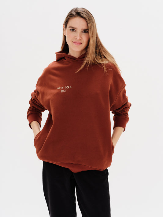 Woman wearing a brown hoodie with a New York Boy embroidery text
