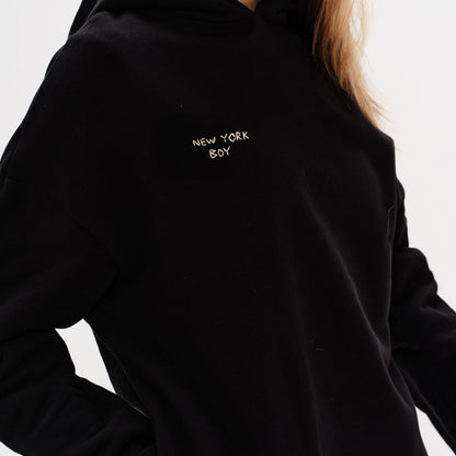 Woman wearing a black hoodie with a New York Boy embroidery text