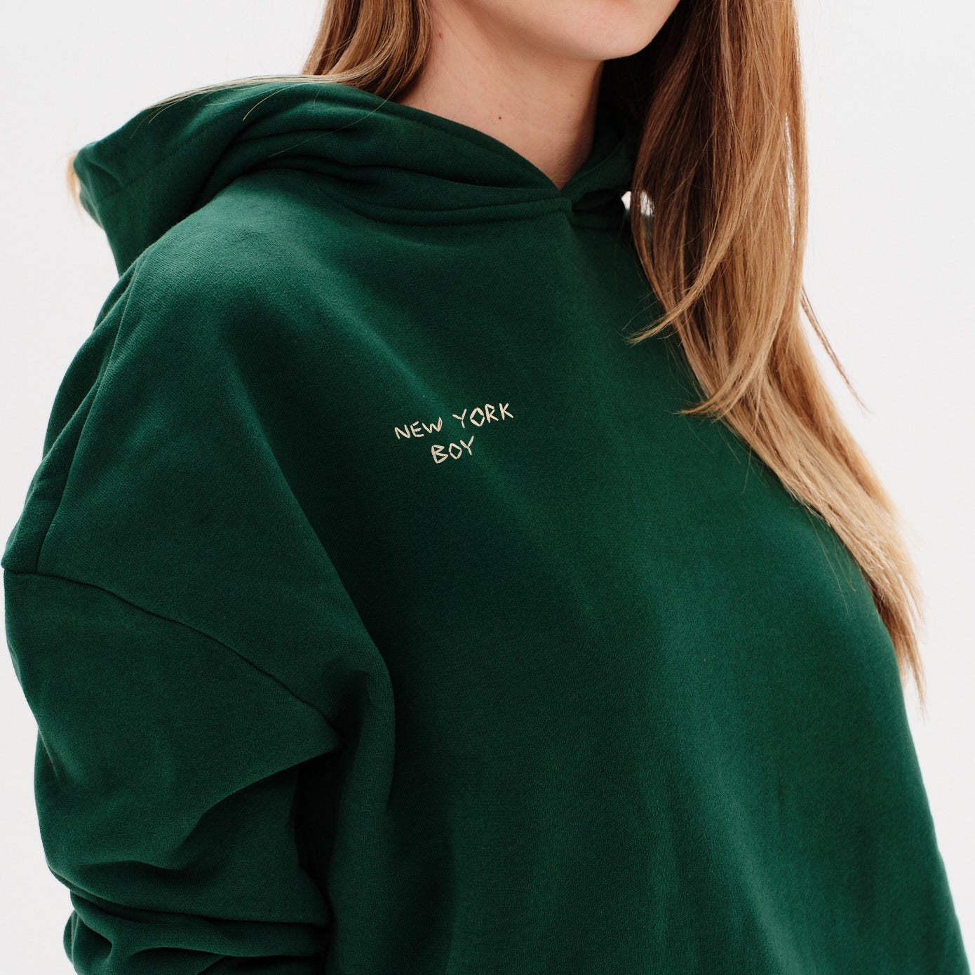 Woman wearing a green hoodie with a New York Boy embroidery text