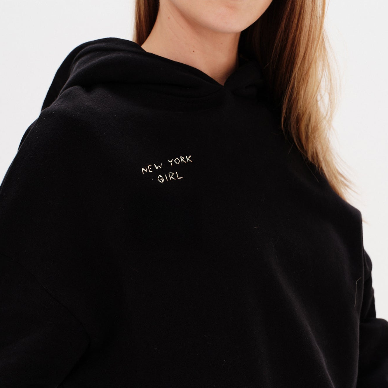 Woman wearing a black hoodie with a New York Girl embroidery.