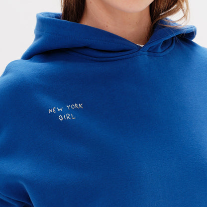 Woman wearing a blue hoodie with a New York Girl embroidery.