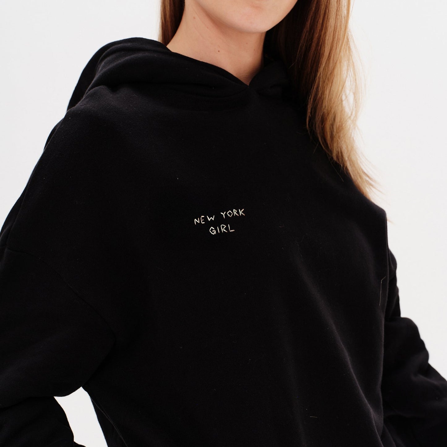 Woman wearing an black hoodie with a New York Girl embroidery.