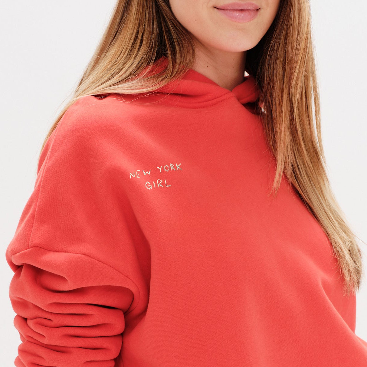 Woman wearing an orange hoodie with a New York Girl embroidery.