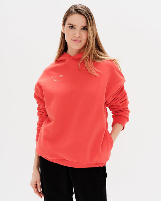 Woman wearing an orange hoodie with a New York Girl embroidery.