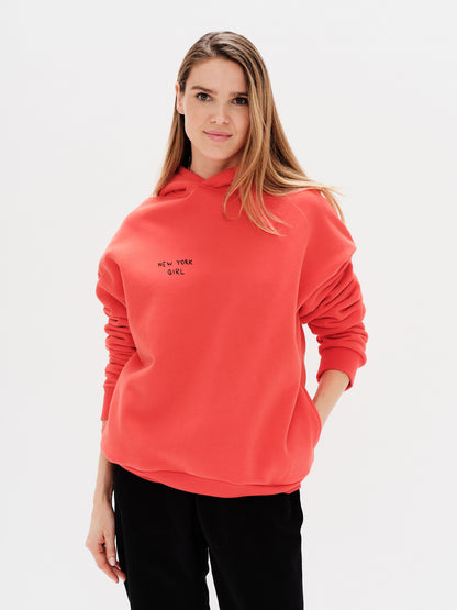 Woman wearing an orange hoodie with a New York Girl embroidery.