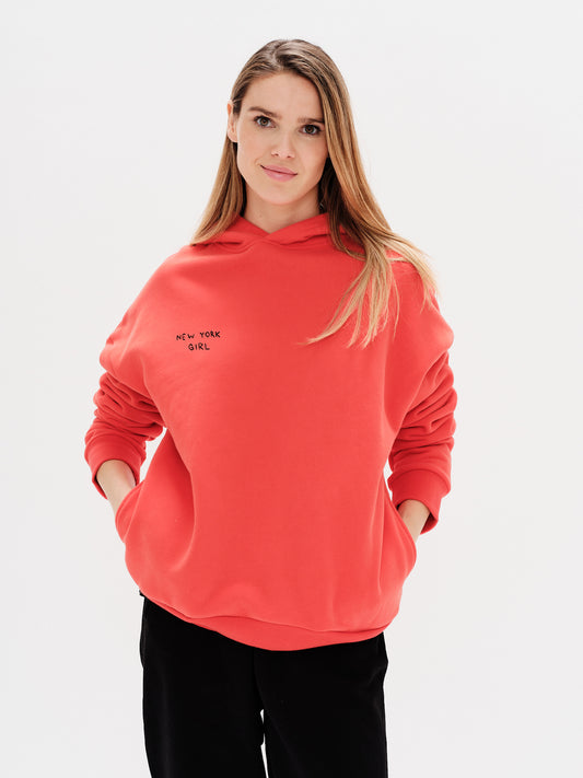 Woman wearing an orange hoodie with a New York Girl embroidery.