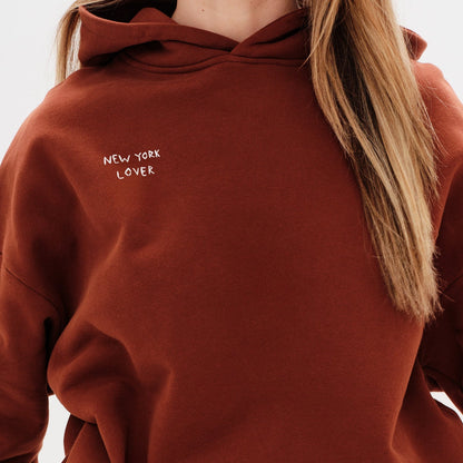 Woman wearing a brown hoodie with New York Lover embroidery text