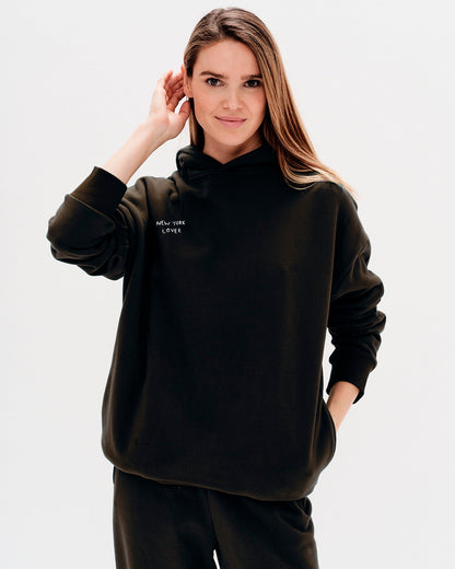 Woman wearing a black hoodie with New York Lover embroidery text