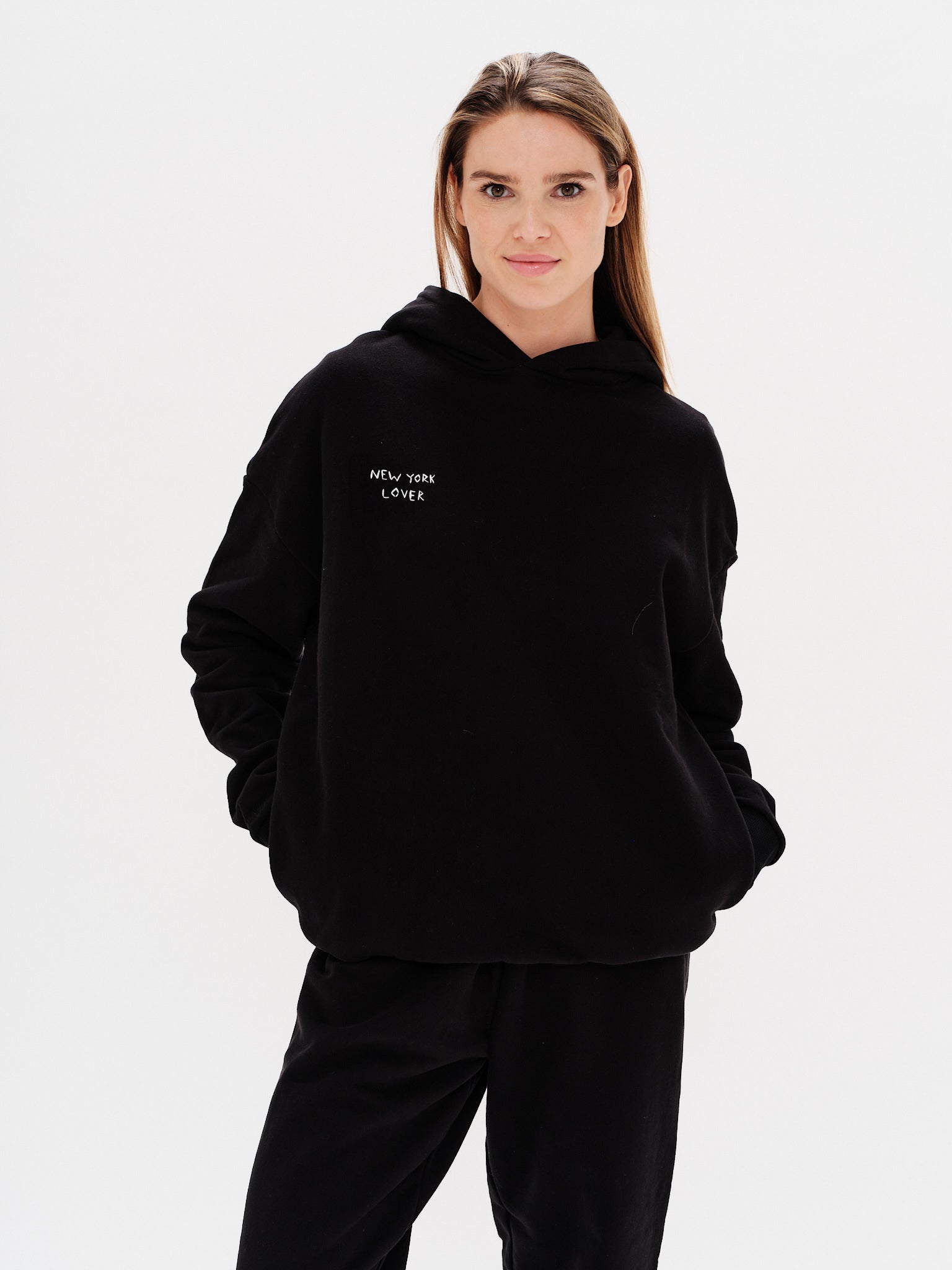 Woman wearing a black hoodie with New York Lover embroidery text