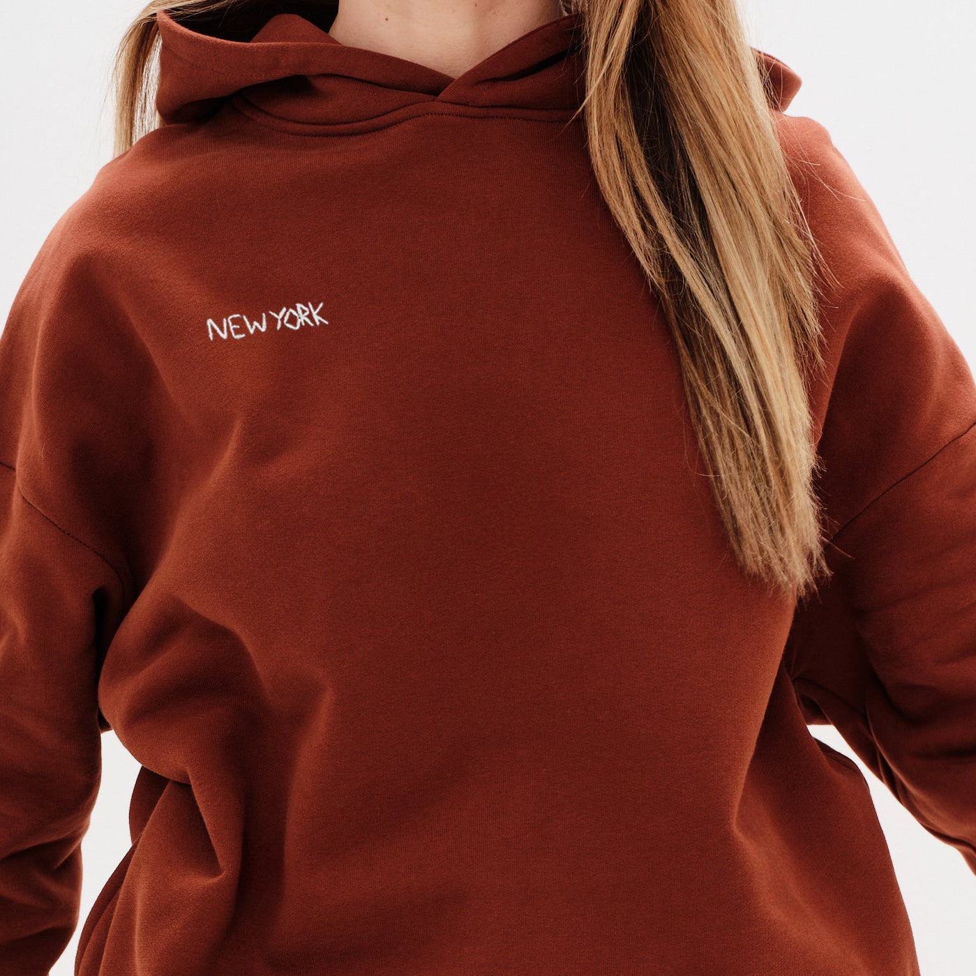 Woman wearing a brown premium hoodie with a 'New York' embroidery