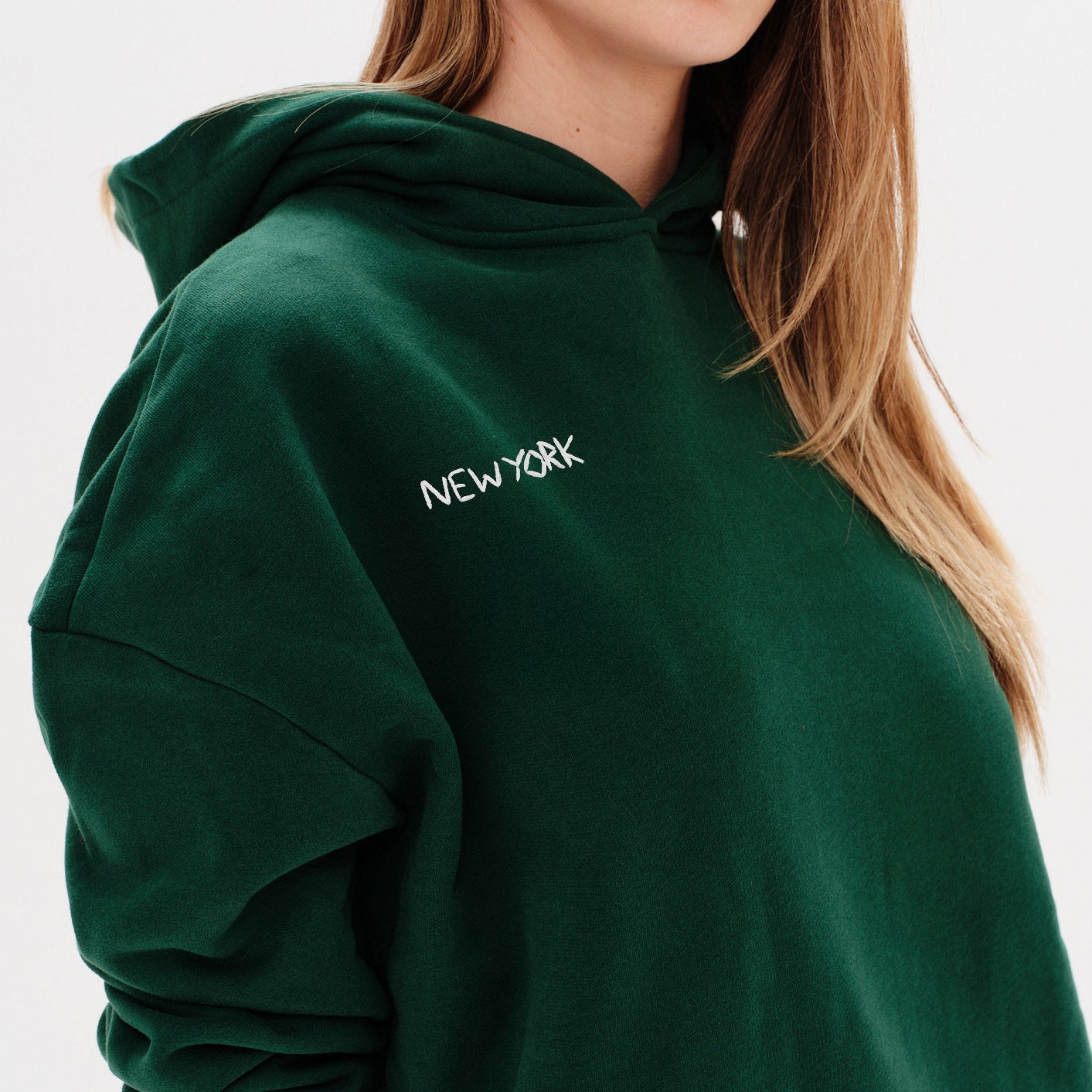 Woman wearing a green premium hoodie with a 'New York' embroidery