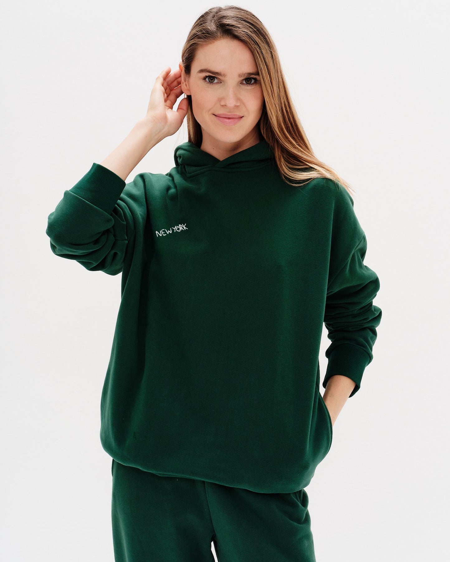 Woman wearing a green premium hoodie with a 'New York' embroidery