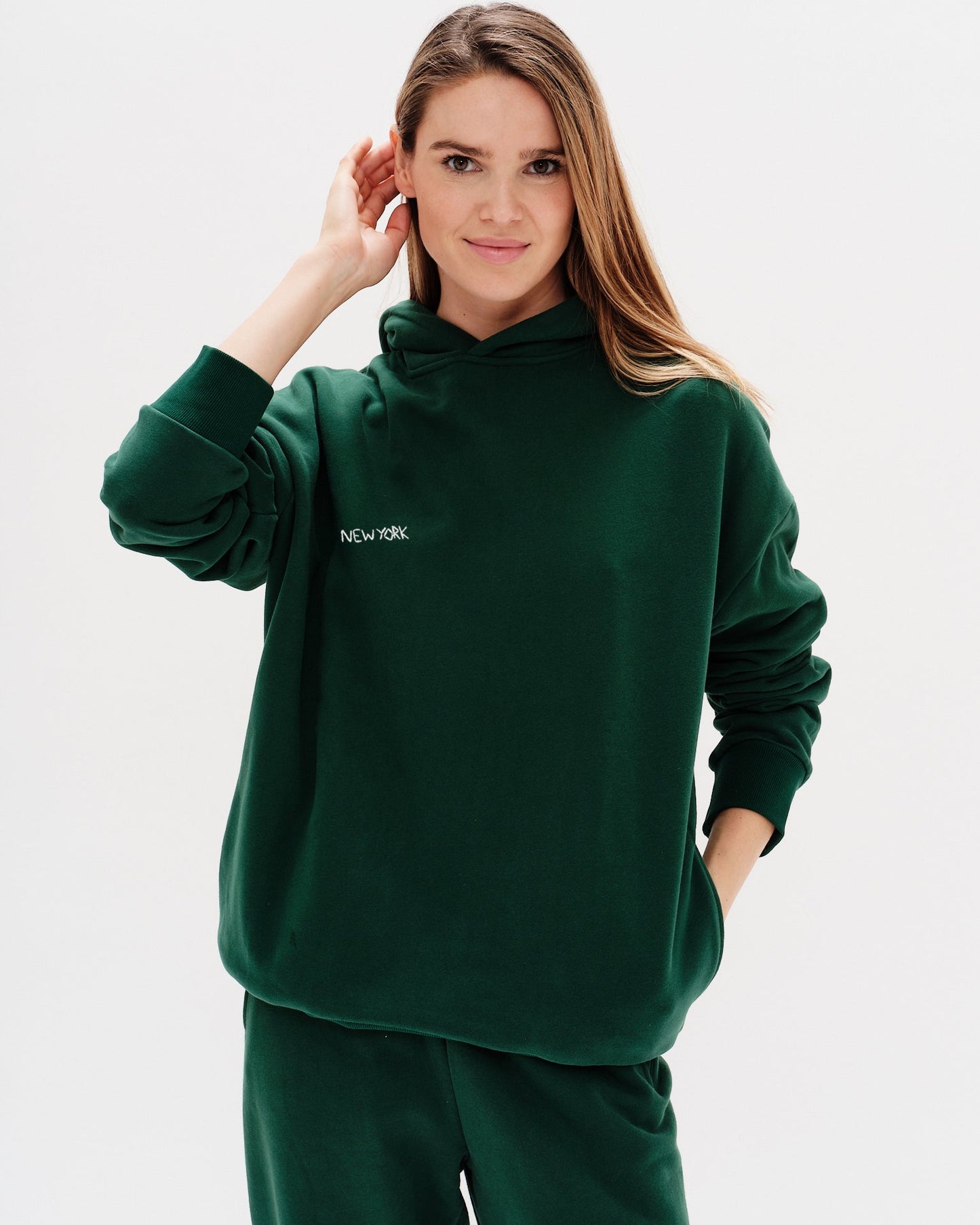 Woman wearing a green premium hoodie with a 'New York' embroidery