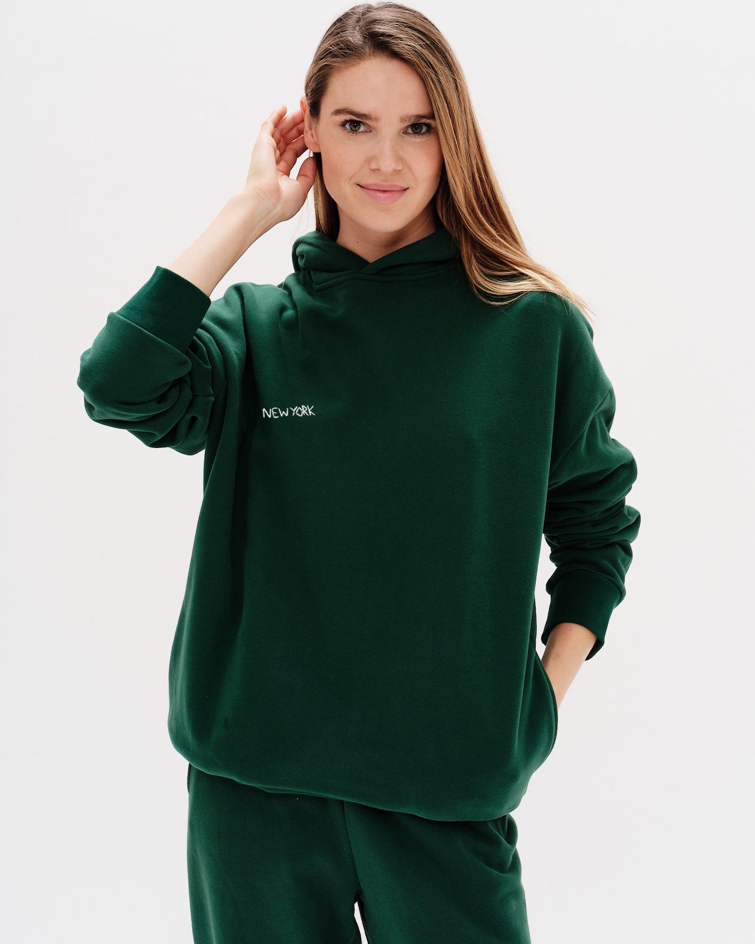 Woman wearing a green premium hoodie with a 'New York' embroidery