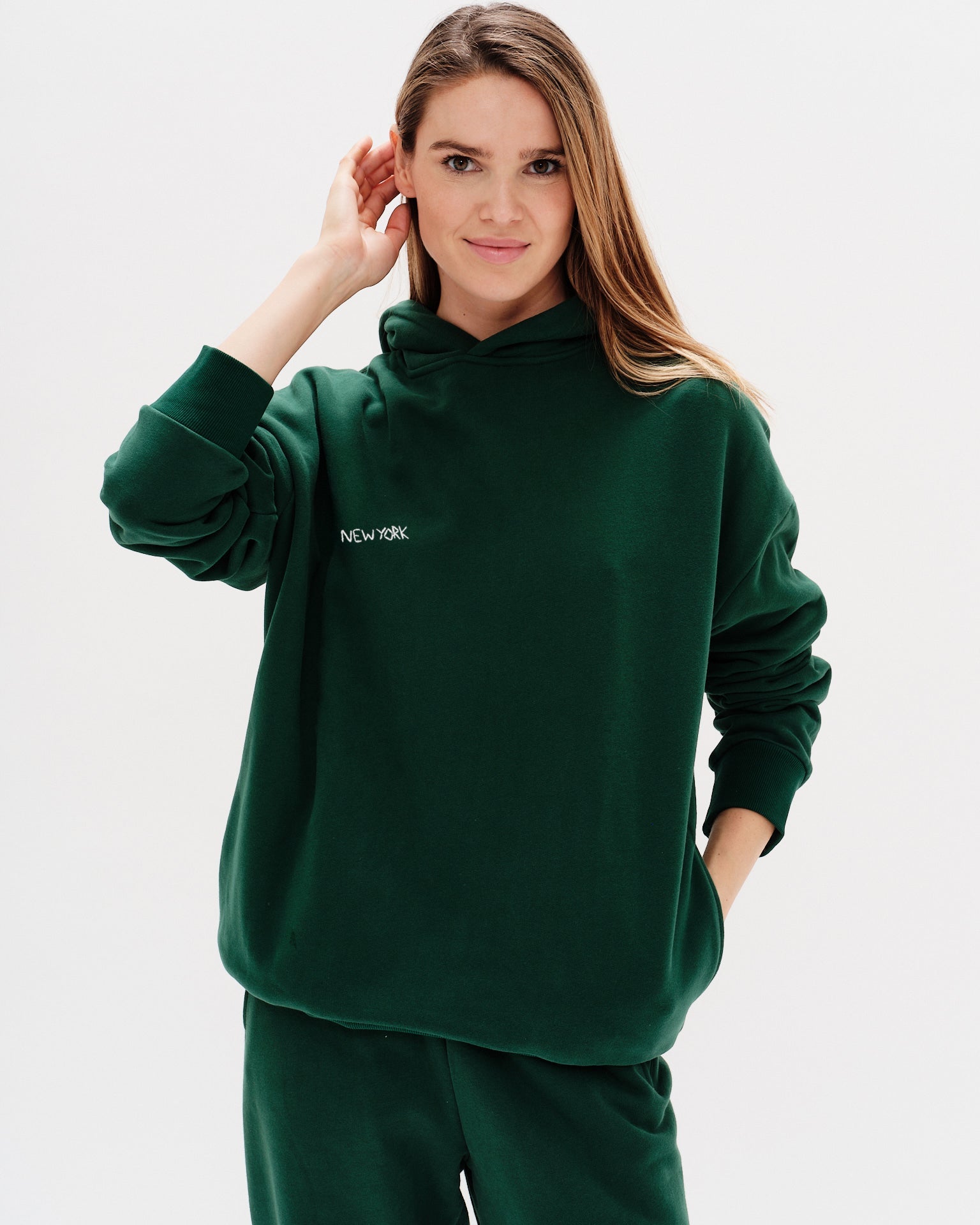 Woman wearing a green premium hoodie with a 'New York' embroidery