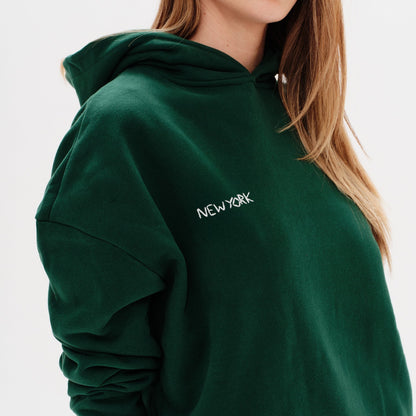 Woman wearing a green premium hoodie with a 'New York' embroidery