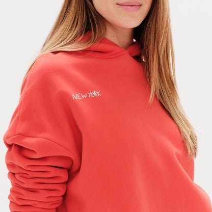Woman wearing an orange premium hoodie with a 'New York' embroidery