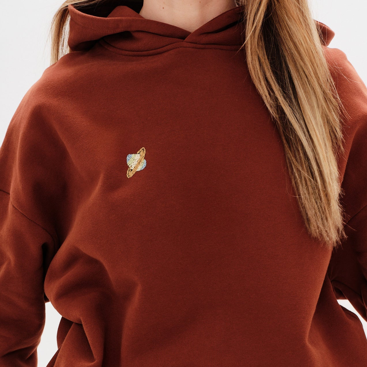 Woman wearing a premium brown hoodie with a planet embroidery
