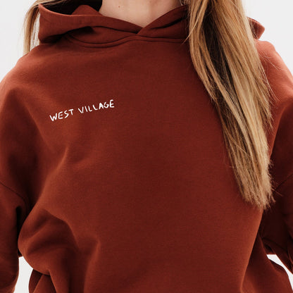 Woman wearing a brown hoodie with a 'West Village' embroidery 