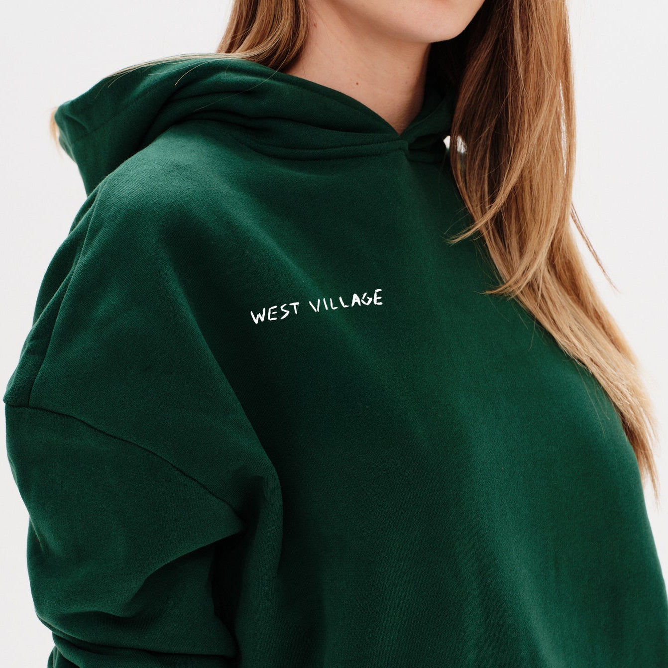 Woman wearing a green hoodie with a 'West Village' embroidery 