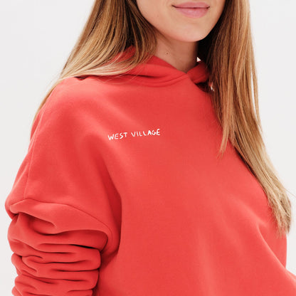 Woman wearing an orange hoodie with a 'West Village' embroidery 