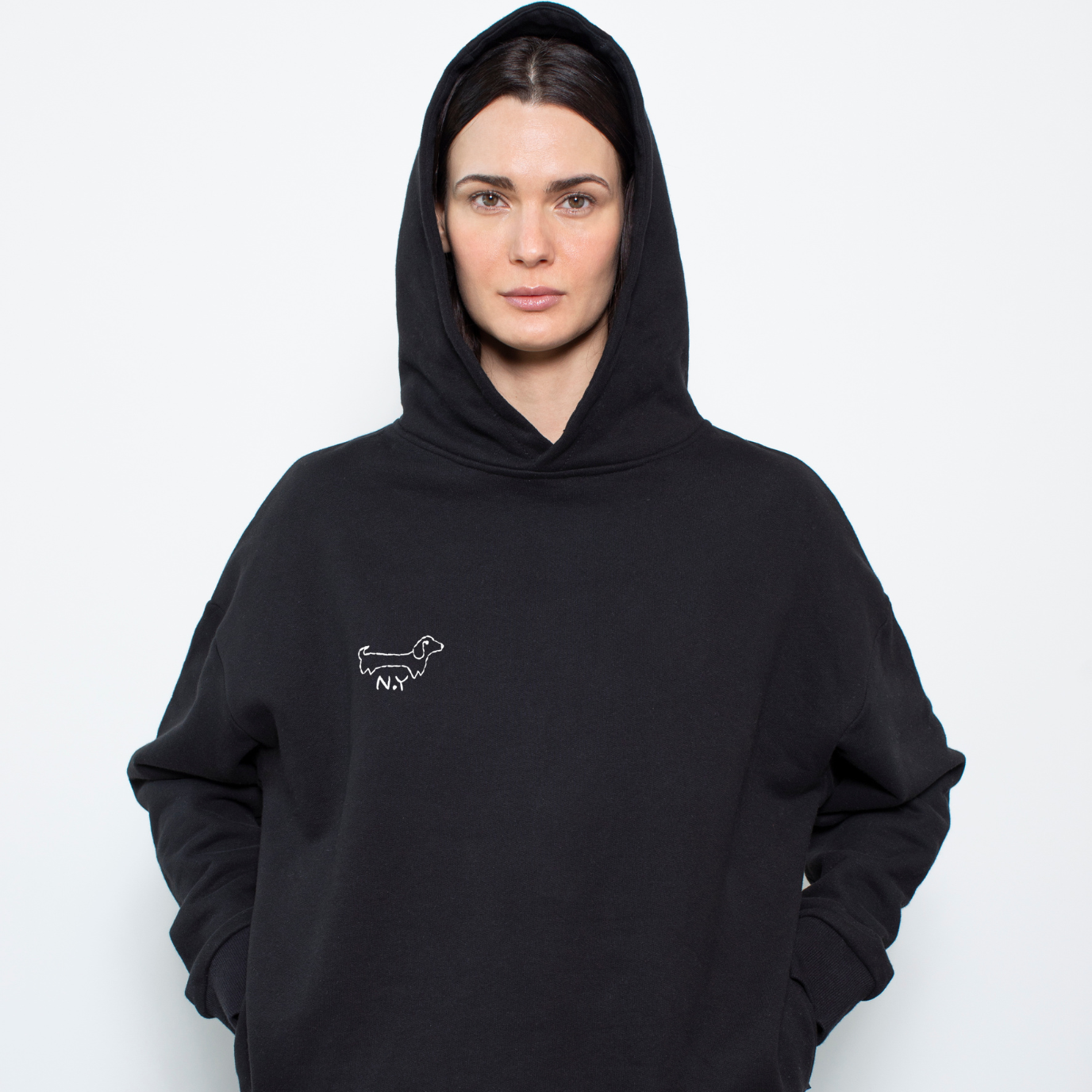 Person wearing a black hoodie with a small dog embroidery on a plain background