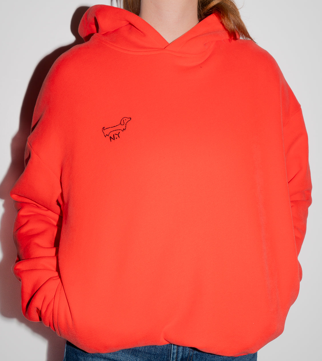 Person wearing an orange hoodie with a small dog embroidery on a plain background