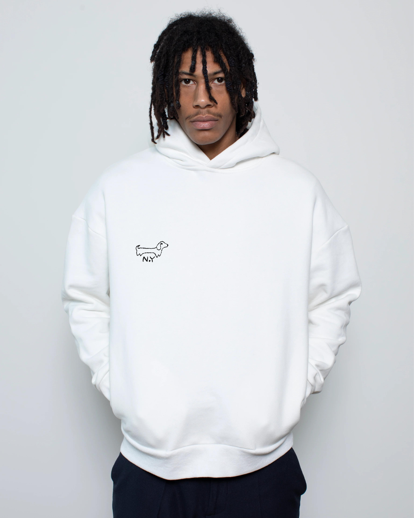 Person wearing a white hoodie with a small dog embroidery on a plain background