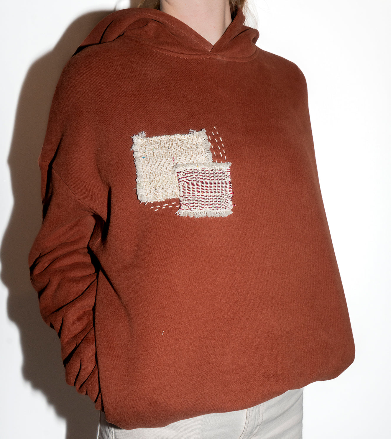 Brown hoodie with a white textured square design on a plain background