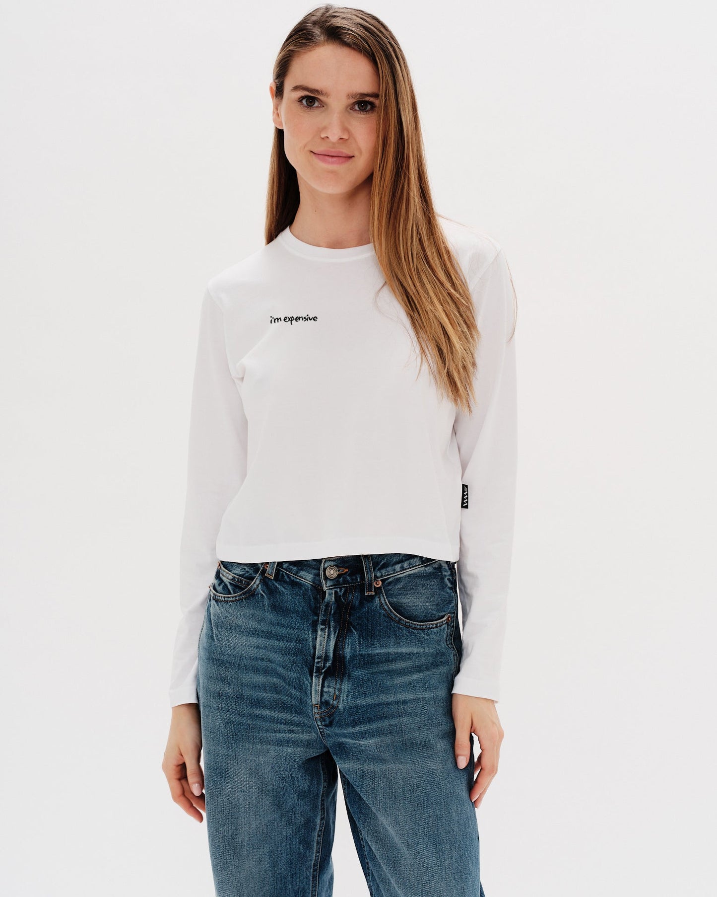 Woman wearing a white long-sleeve t-shirt with an I'm expensive embroidery