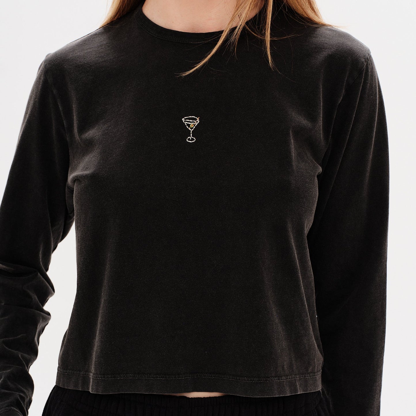 Woman wearing a black long-sleeve crop top with a Martini design embroidery