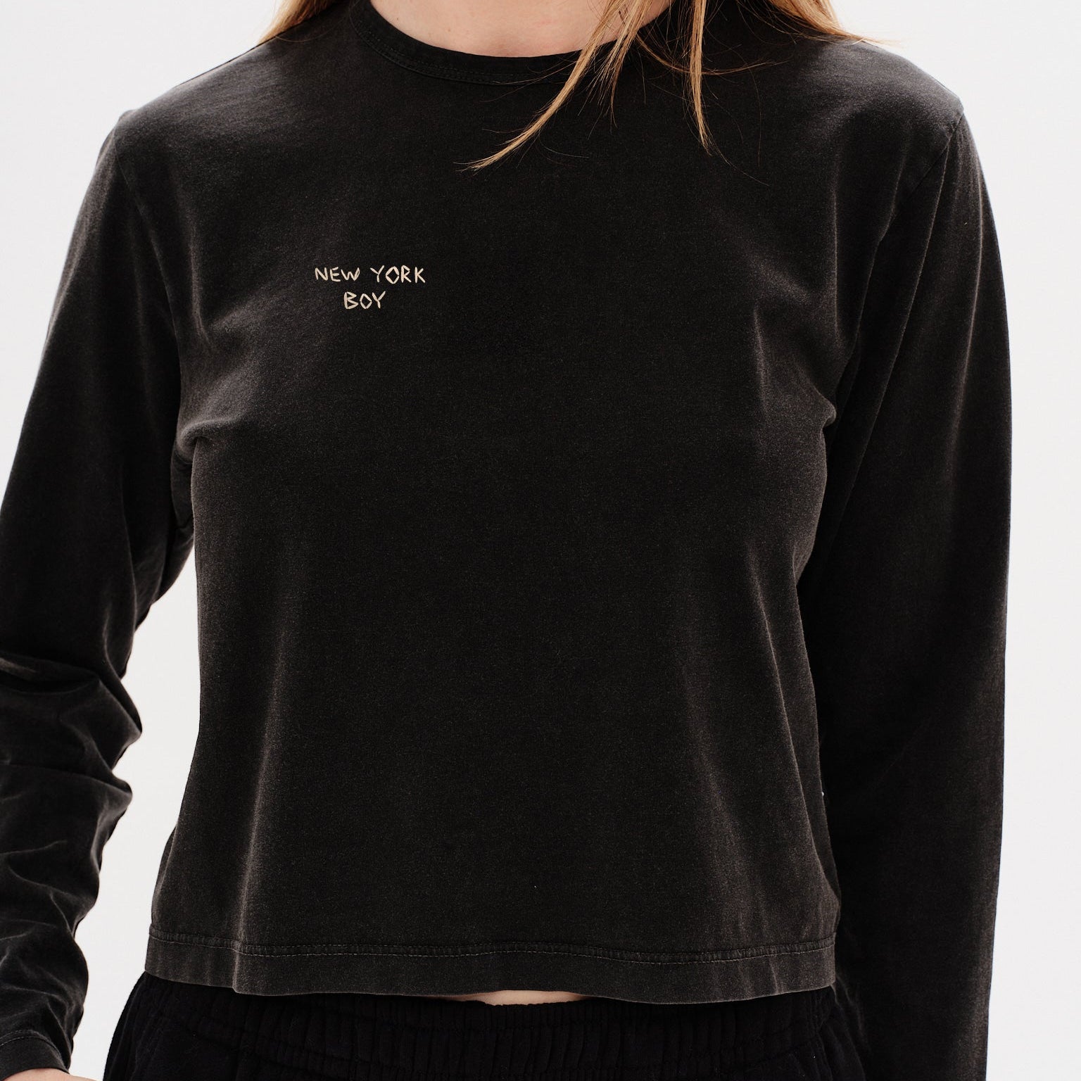 Woman wearing a black long-sleeve crop top with 'New York Boy' embroidery