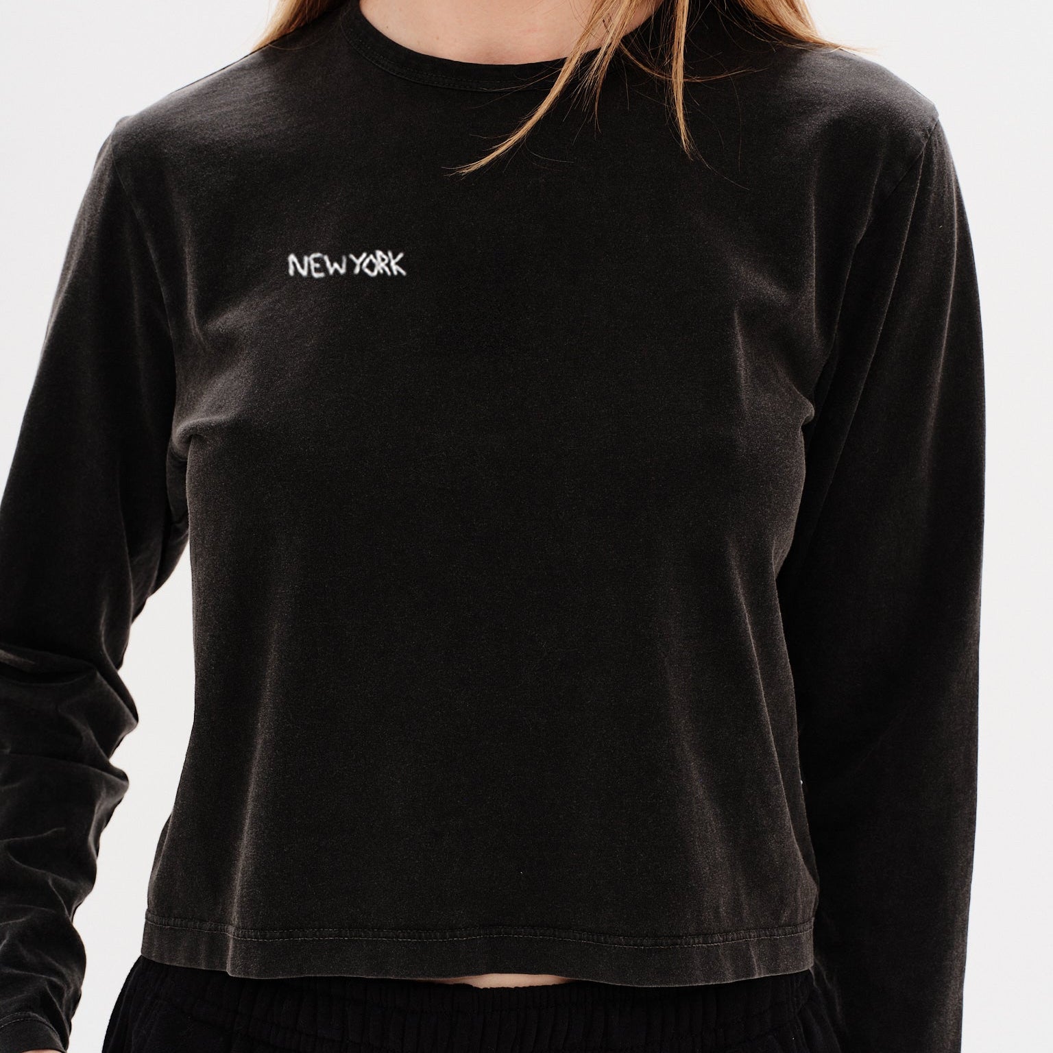 Woman wearing a black long-sleeve crop top with a New York embroidery