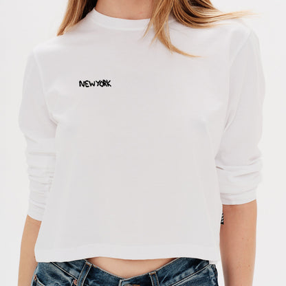 Woman wearing a white long-sleeve crop top with a New York embroidery