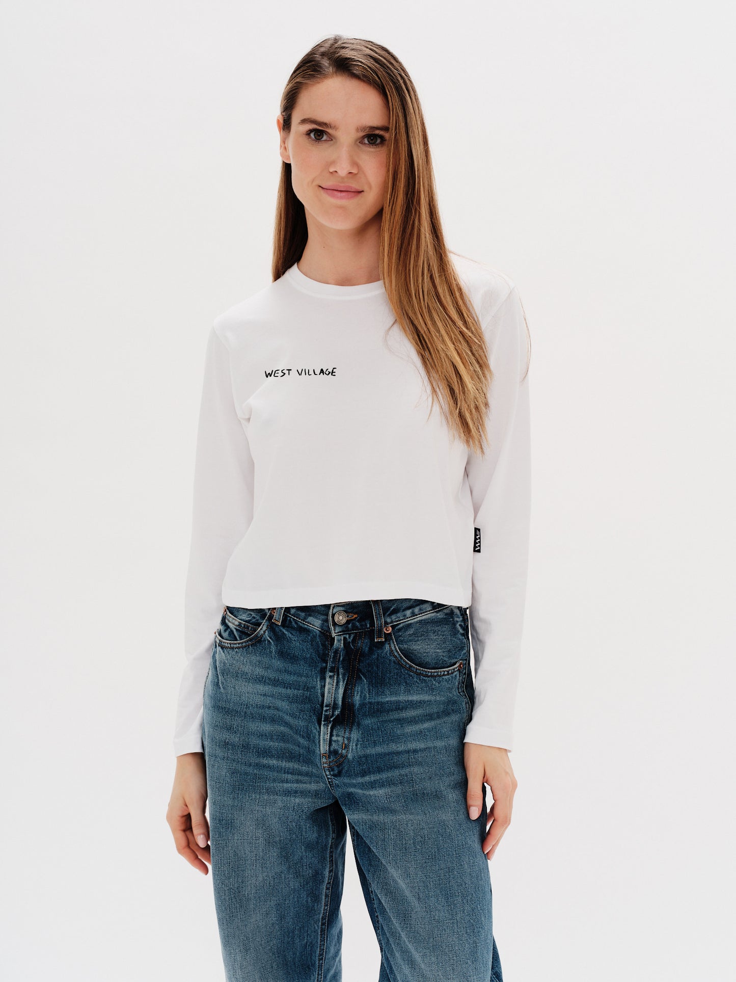 Woman wearing a white long-sleeve t-shirt with a west village embroidery