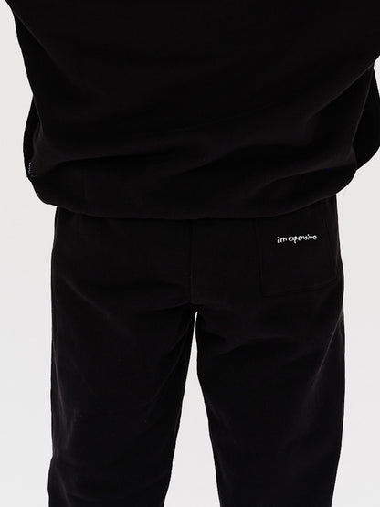 Woman wearing black pants with I'm Expensive embroidery