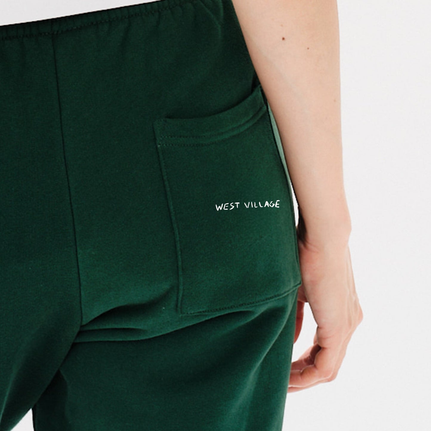 Woman wearing green pants with West Village embroidery
