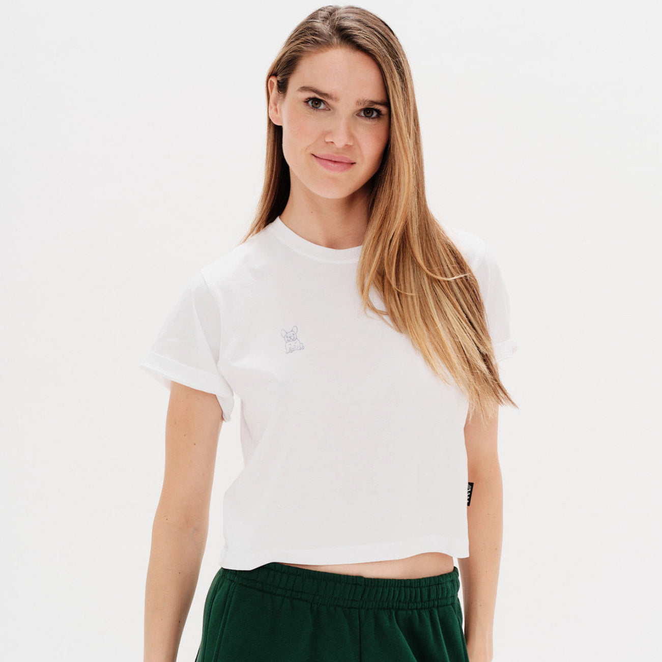Woman wearing a white t-shirt with a small bulldog embroidery on a plain background
