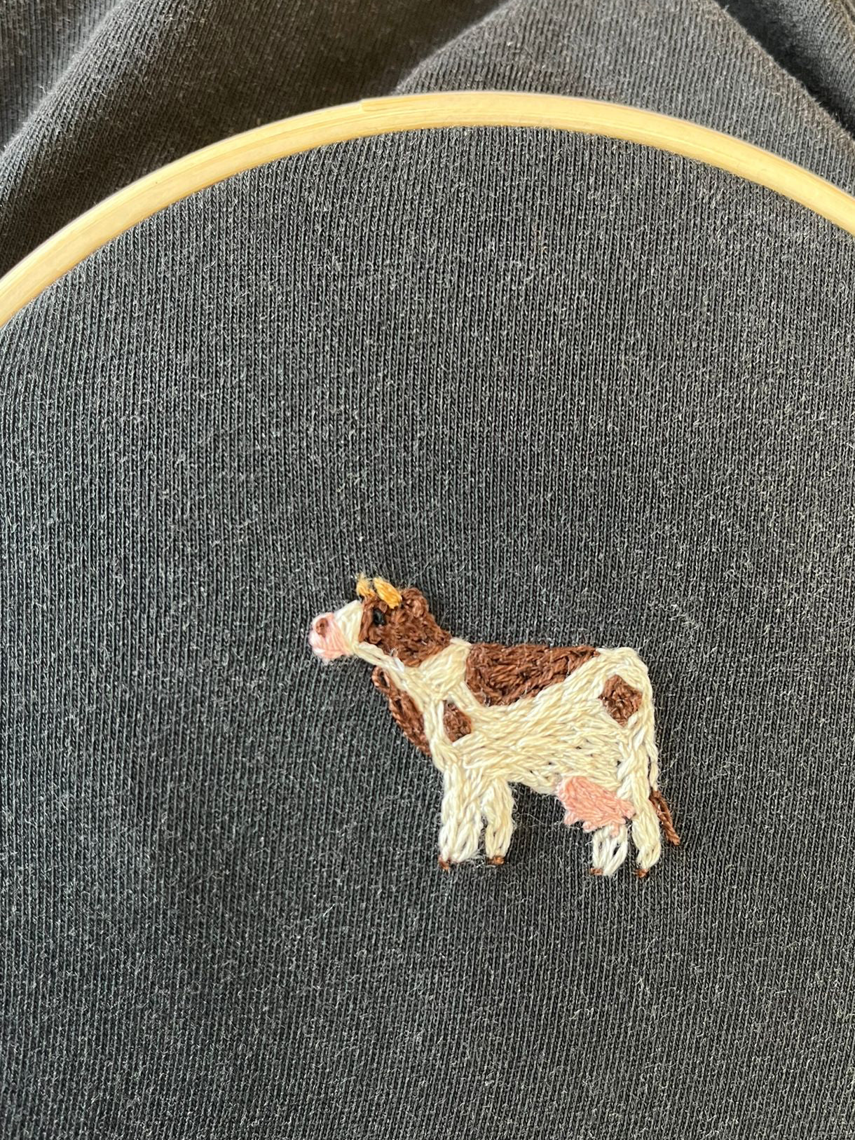 Embroidery hoop with a cow design on dark fabric